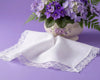 White lace-trimmed handkerchiefs on a purple surface with a vase of purple flowers.