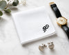 White handkerchief with initials, watch, and cufflinks on a marble surface.