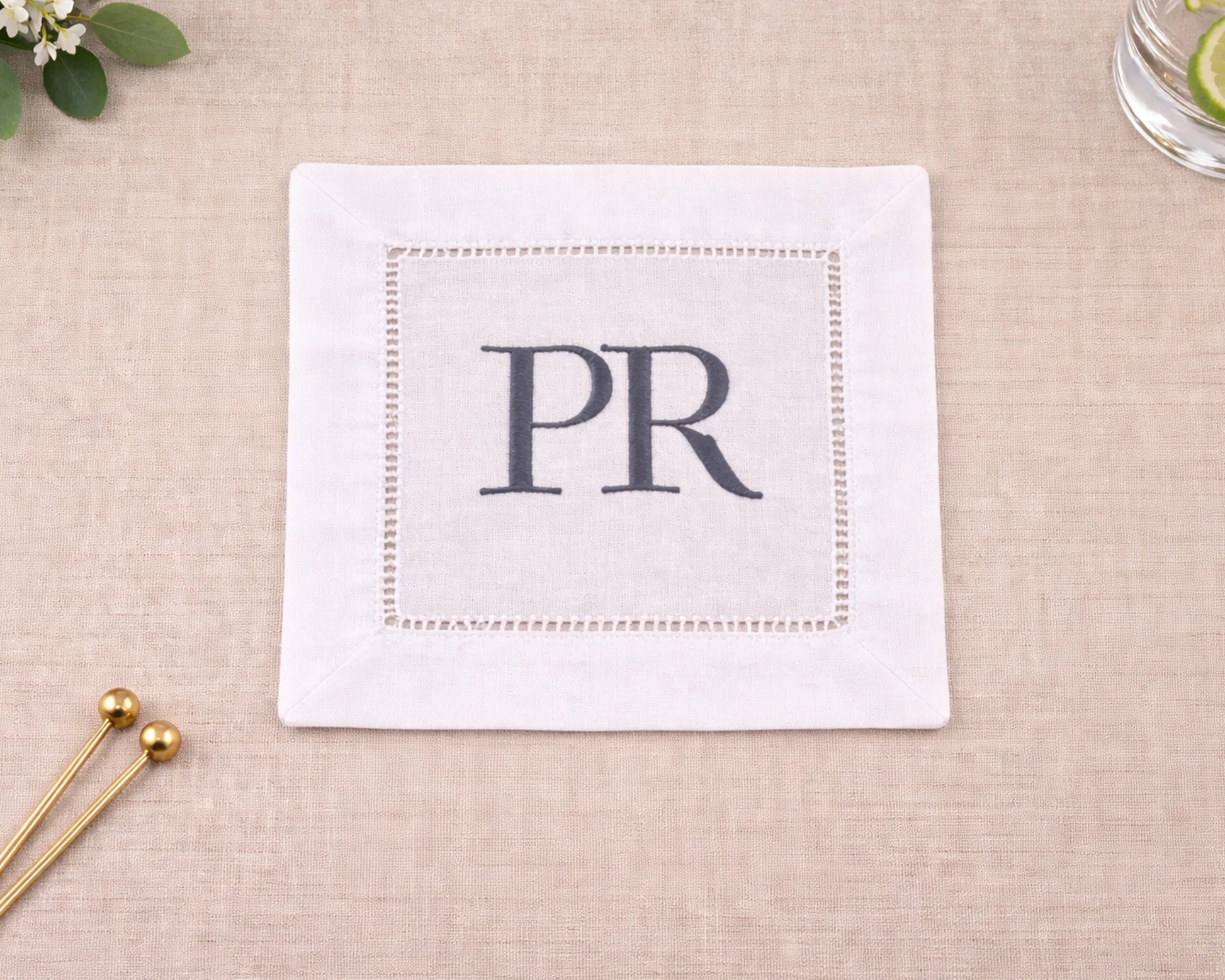 White napkin with 'PR' monogram on a beige surface with decorative elements.