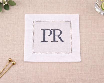 White napkin with 'PR' monogram on a beige surface with decorative elements.