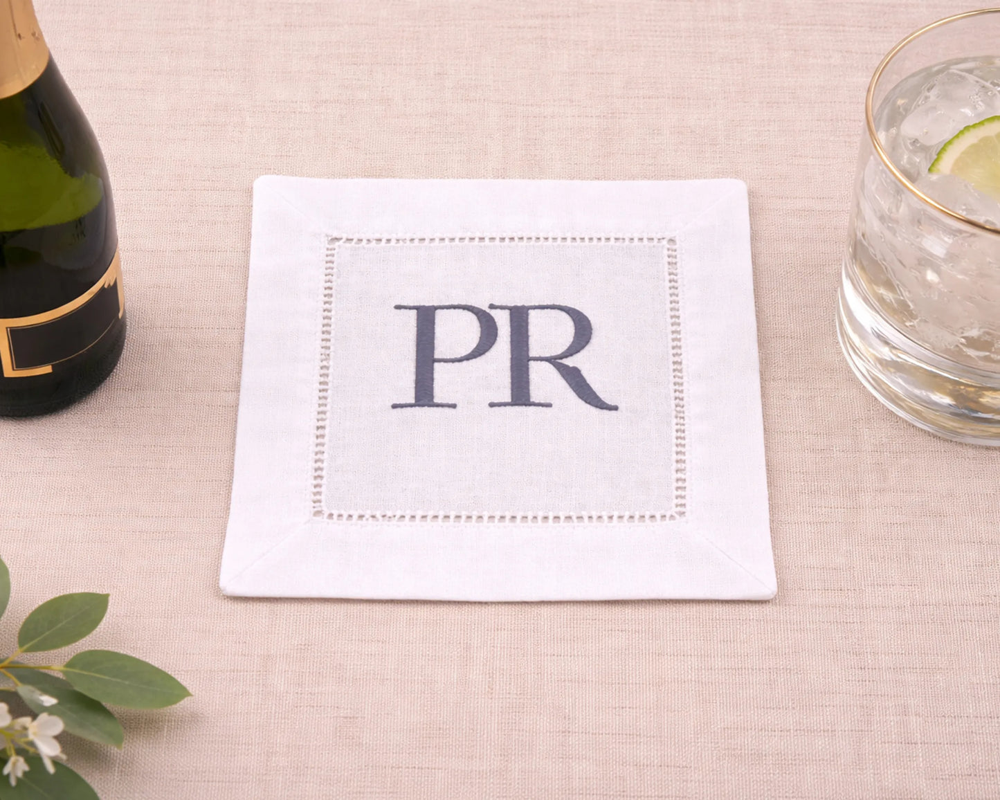 White napkin with 'PR' monogram on a table with a bottle and glass.