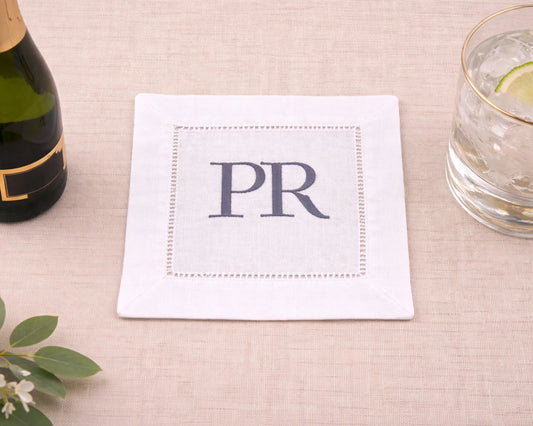 White napkin with 'PR' monogram on a table with a bottle and glass.