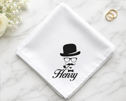 White napkin with a black design of a face wearing a top hat, glasses, and a mustache, with 'Henry' written below on a marble surface.
