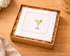 White napkin with a cocktail design in a brown box on a wooden surface