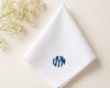 White napkin with blue monogram on a beige surface with white flowers.