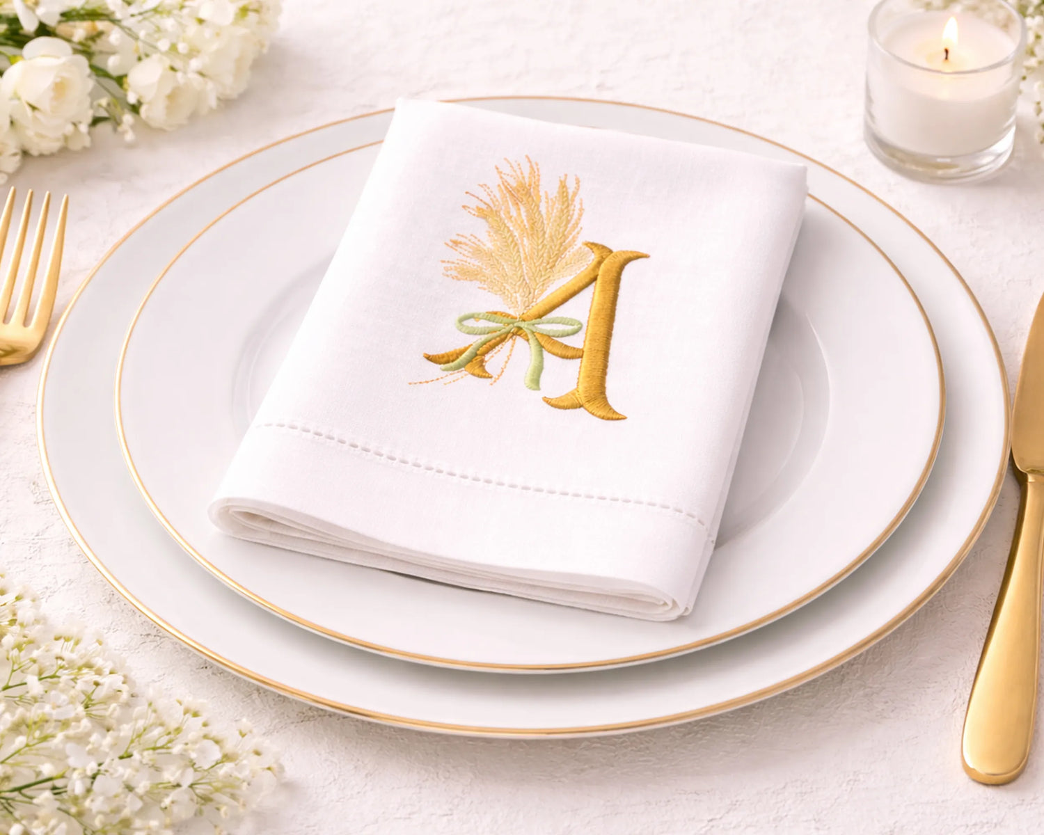 White napkin with gold letter 'M' design on a white plate with gold rim, surrounded by flowers and cutlery.