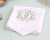 White napkin with green monogram on a light green surface with a fork and decorative elements.