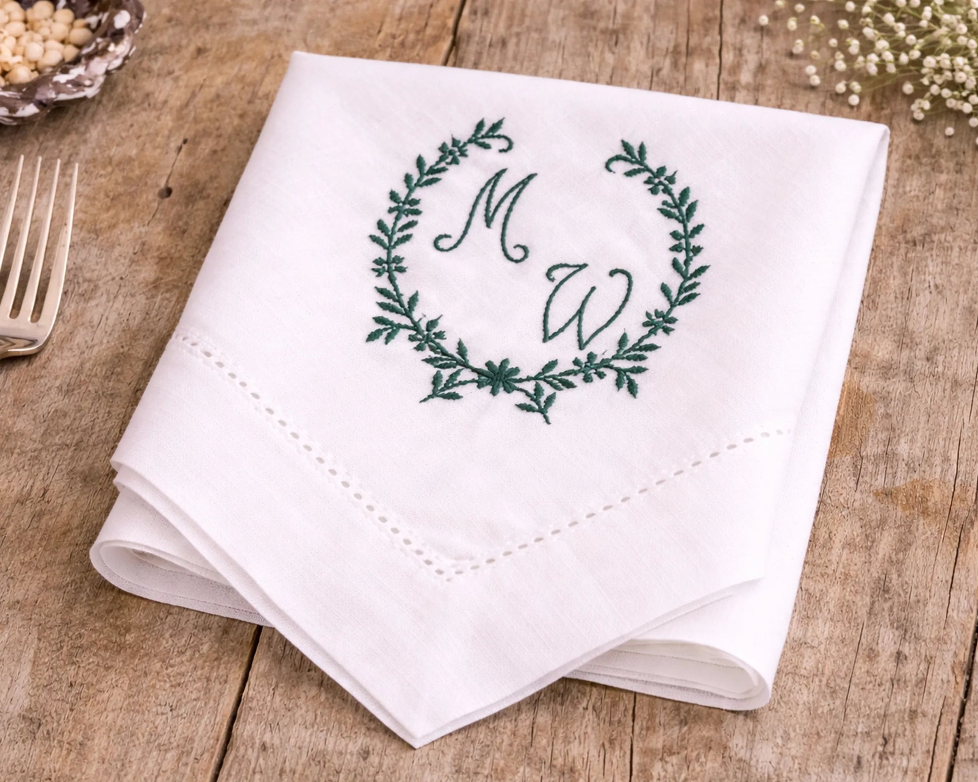 White napkin with green monogram design on a wooden surface