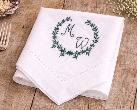 White napkin with green monogram design on a wooden surface