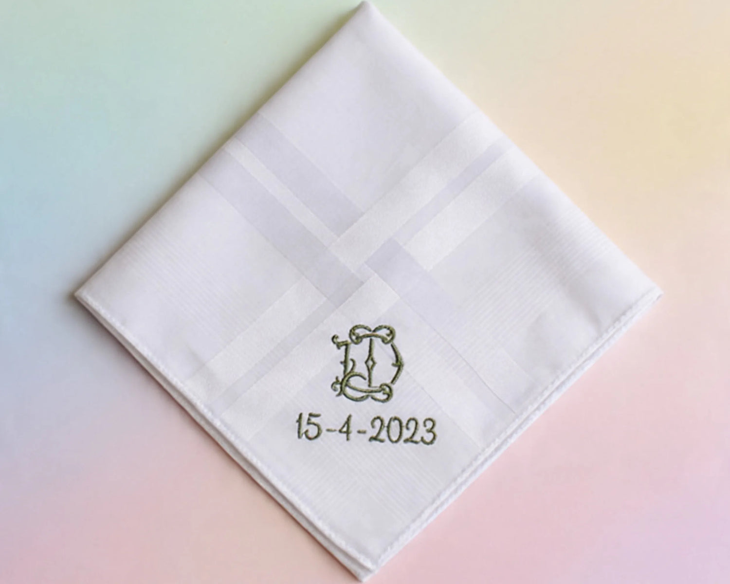 White quilted handkerchief with monogram 'D' and date '15-4-2023' on a pastel gradient background