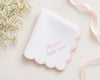 White scalloped-edged hanky with pink text on a light background with flowers and ribbon.