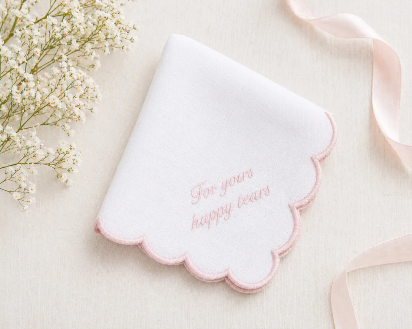 White scalloped-edged hanky with pink text on a light background with flowers and ribbon.