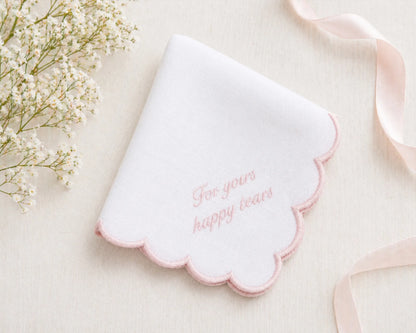 White scalloped-edged hanky with pink text on a light background with flowers and ribbon.