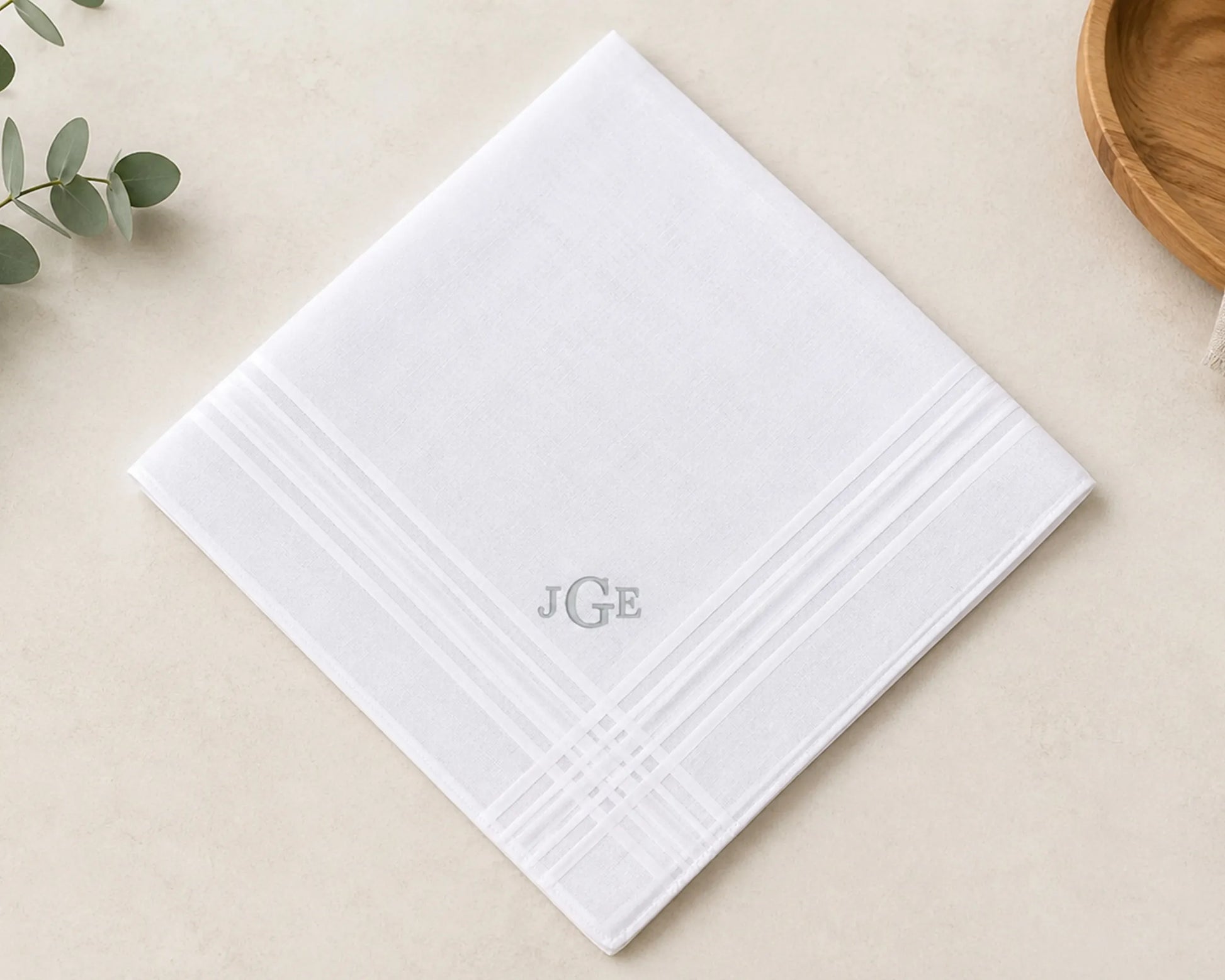 White textured hanky with 'JGE' monogram on a beige surface