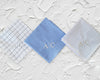 Close up of blue solid and grid patterned cotton handkerchiefs with bold black CSL monogram embroidery.