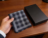 Hand holding a gray checkered pocket square next to a black box on a wooden surface