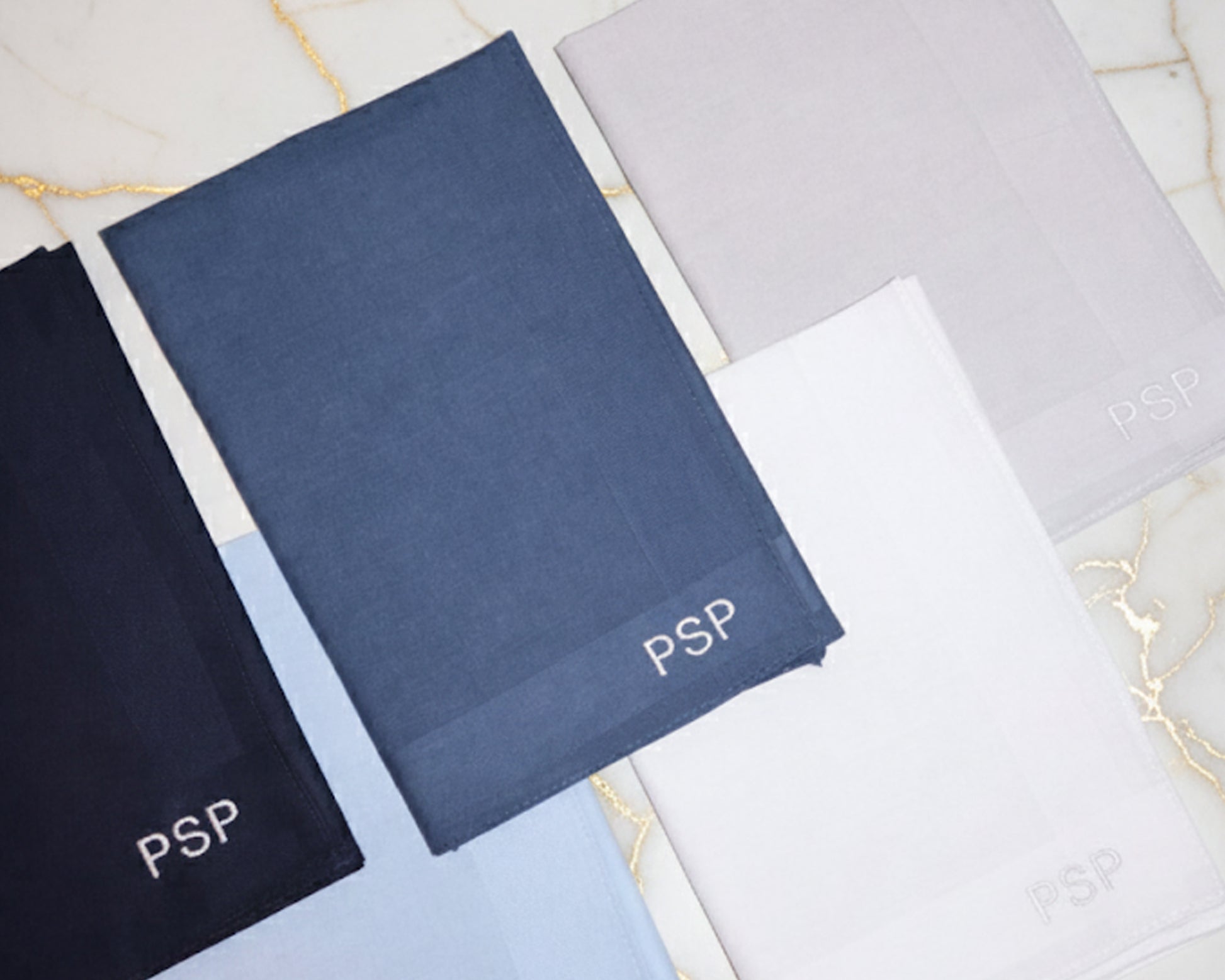 Three personalized cotton handkerchiefs in navy and sky blue featuring custom gold diamond CPM monogram embroidery.
