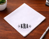 Beige hanky with embroidered design and text, surrounded by flowers on a light background