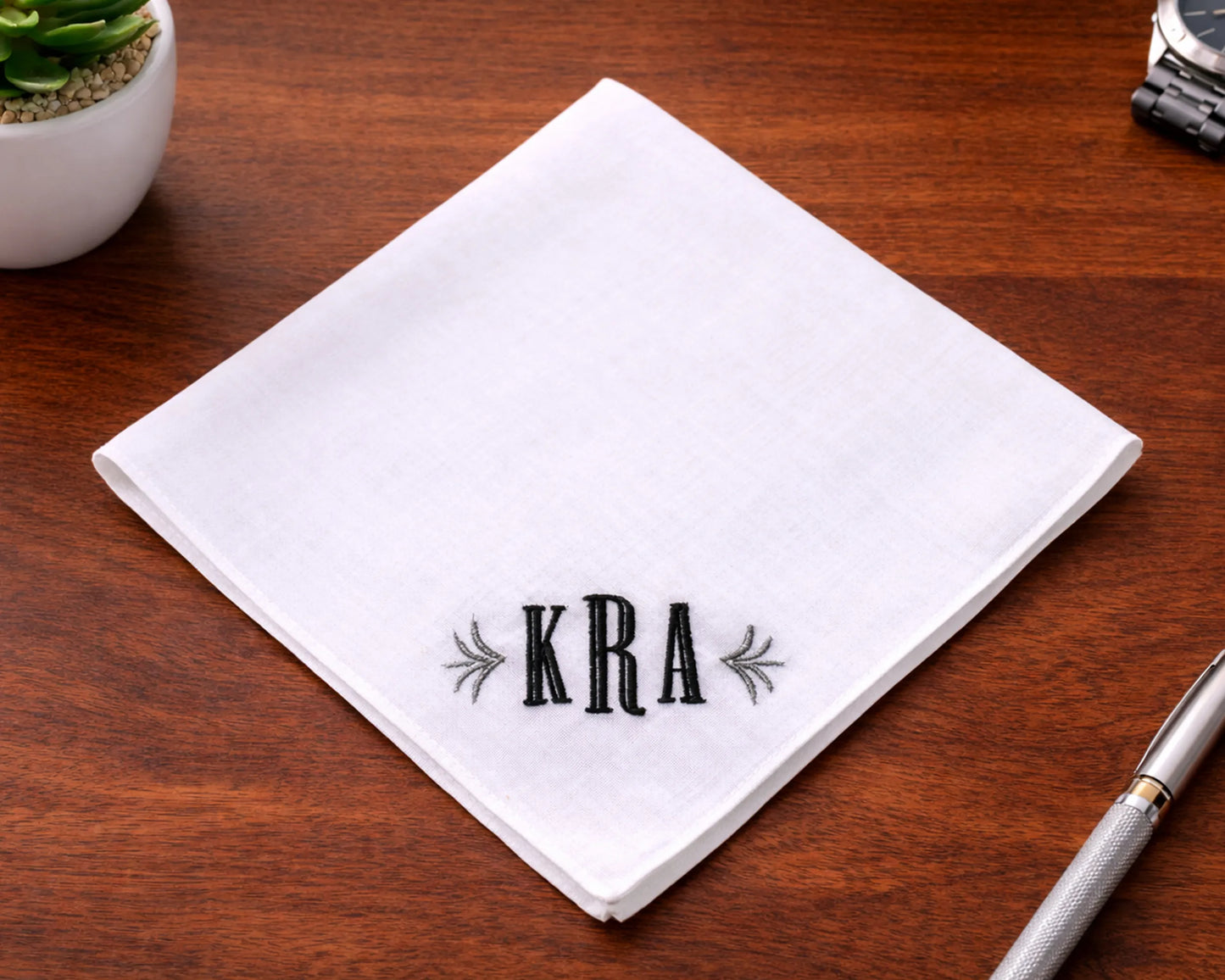 Beige hanky with embroidered design and text, surrounded by flowers on a light background
