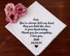 hanky with heartfelt message to a father, accompanied by pink flowers on a wooden surface
