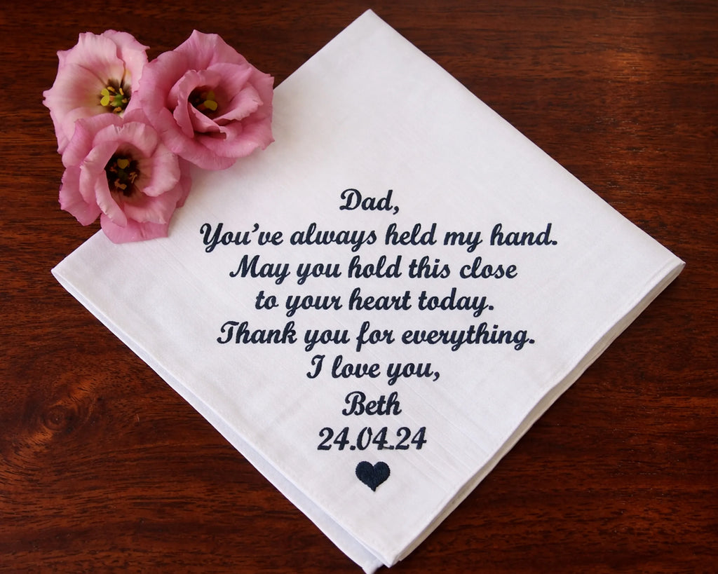 hanky with heartfelt message to a father, accompanied by pink flowers on a wooden surface