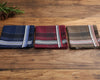Three plaid pocket squares on a wooden surface with greenery.