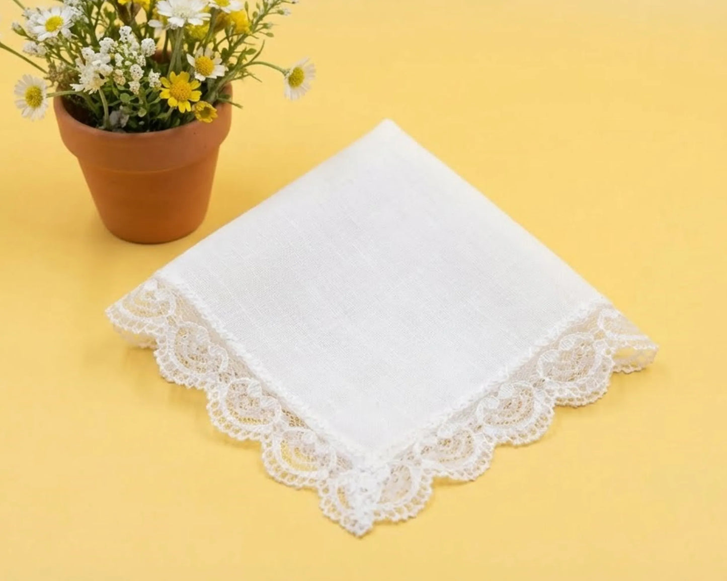 White lace-trimmed handkerchief on a yellow background with a potted plant.