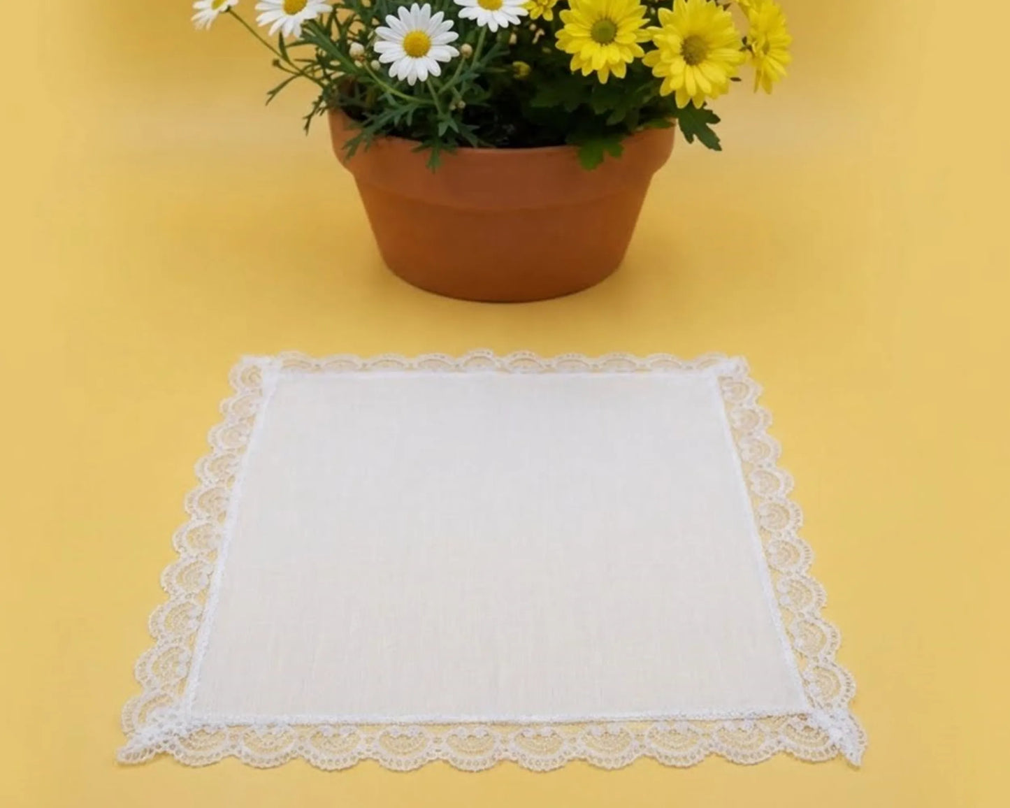 White lace doily on a yellow surface with a potted plant of flowers.