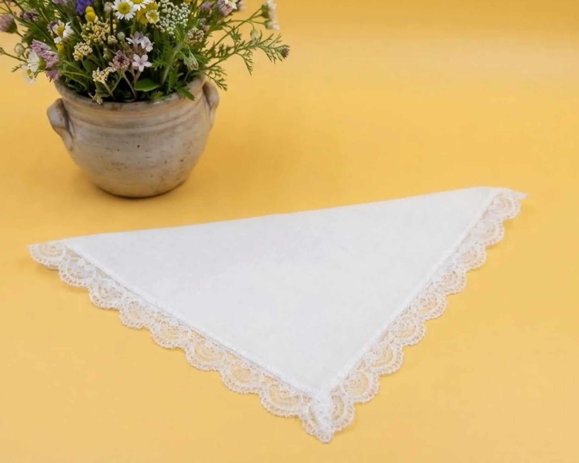 White lace doily on a yellow surface with a pot of flowers.