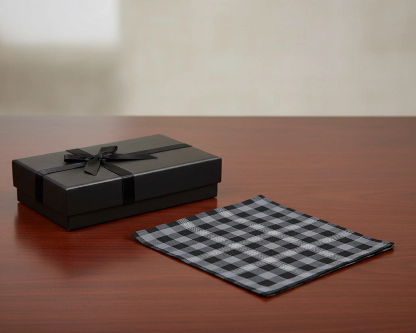 Black gift box with a bow and checkered cloth on a wooden surface