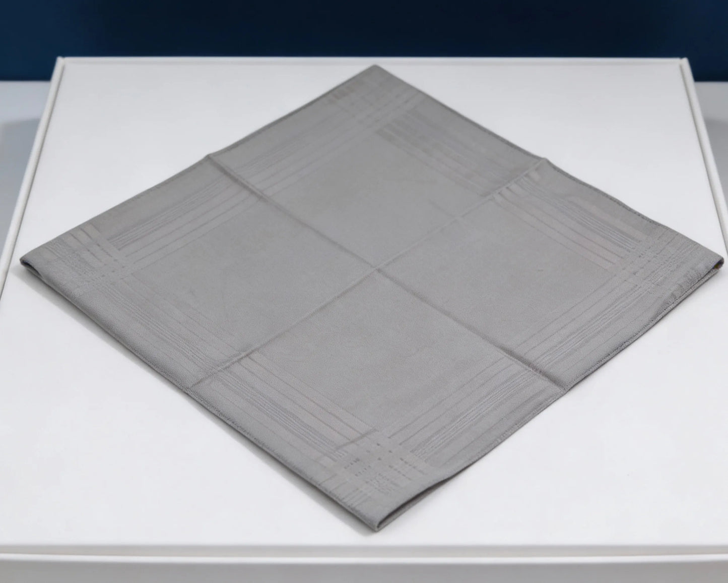 Gray textured square mat on a white surface with a dark blue background