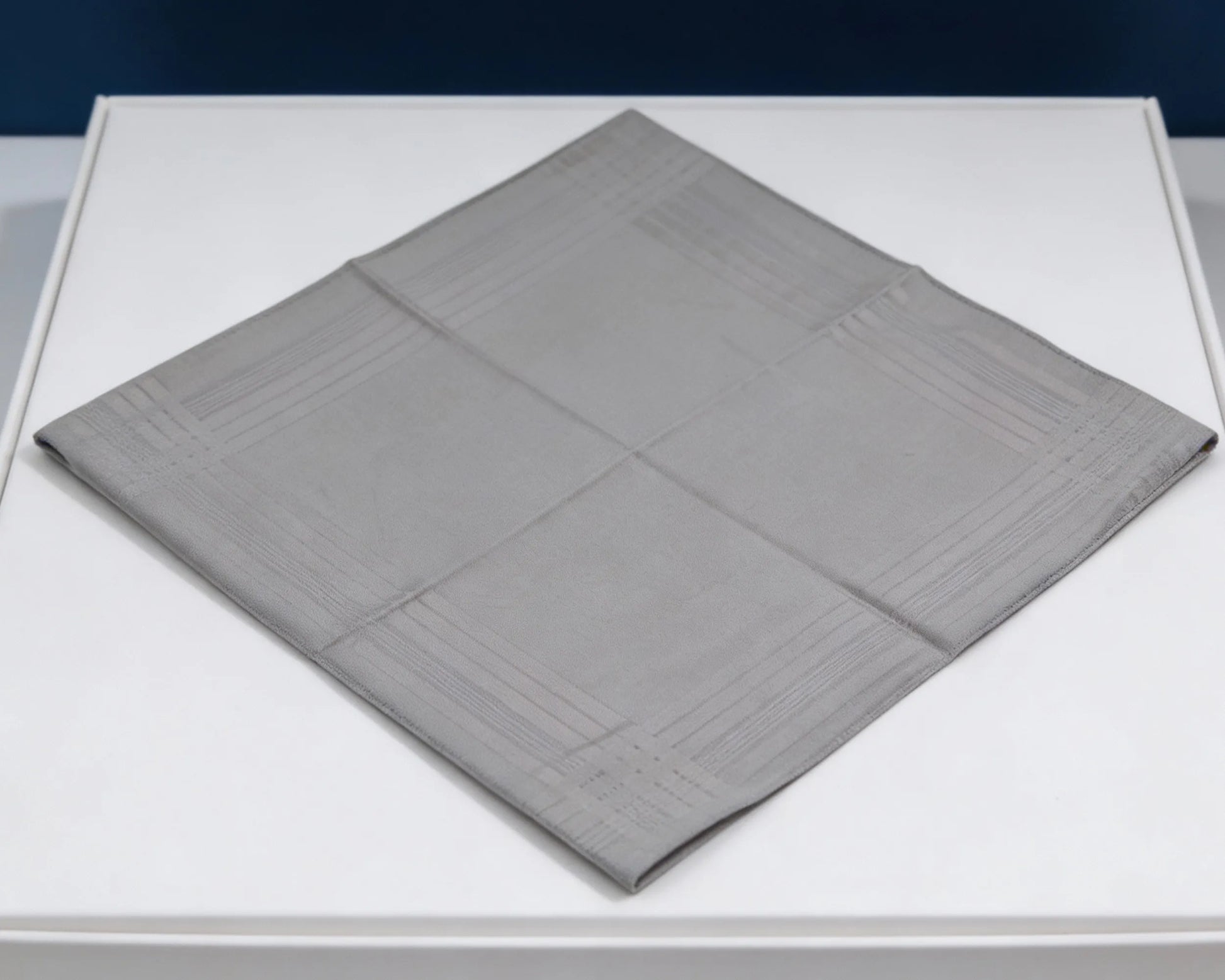 Gray textured square mat on a white surface with a dark blue background