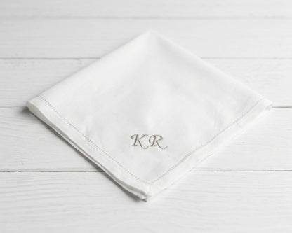 White napkin with 'KR' monogram on a light wooden surface