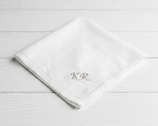 White napkin with 'KR' monogram on a light wooden surface