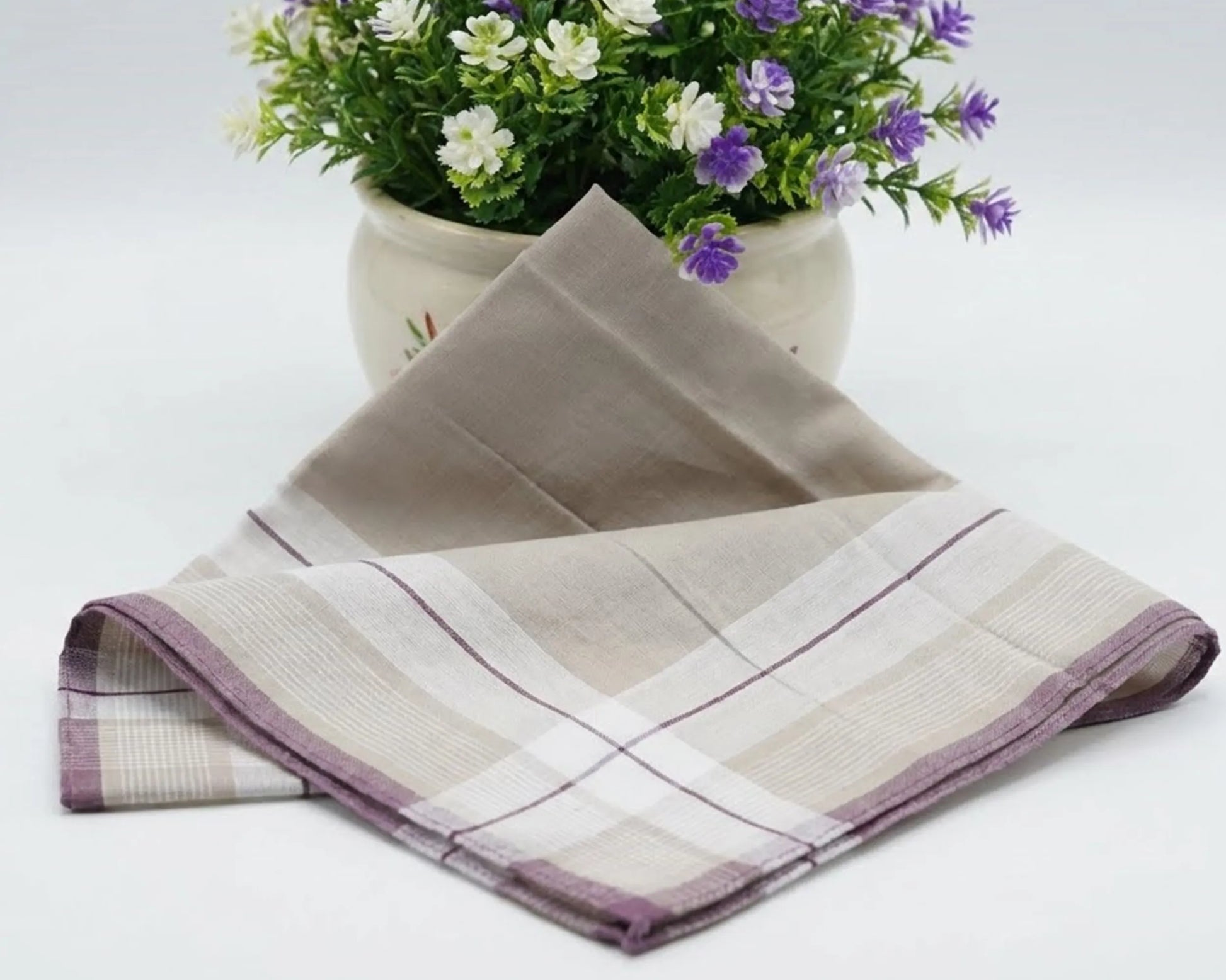 Textured fabric with plaid pattern on a white surface, with a potted plant in the background.