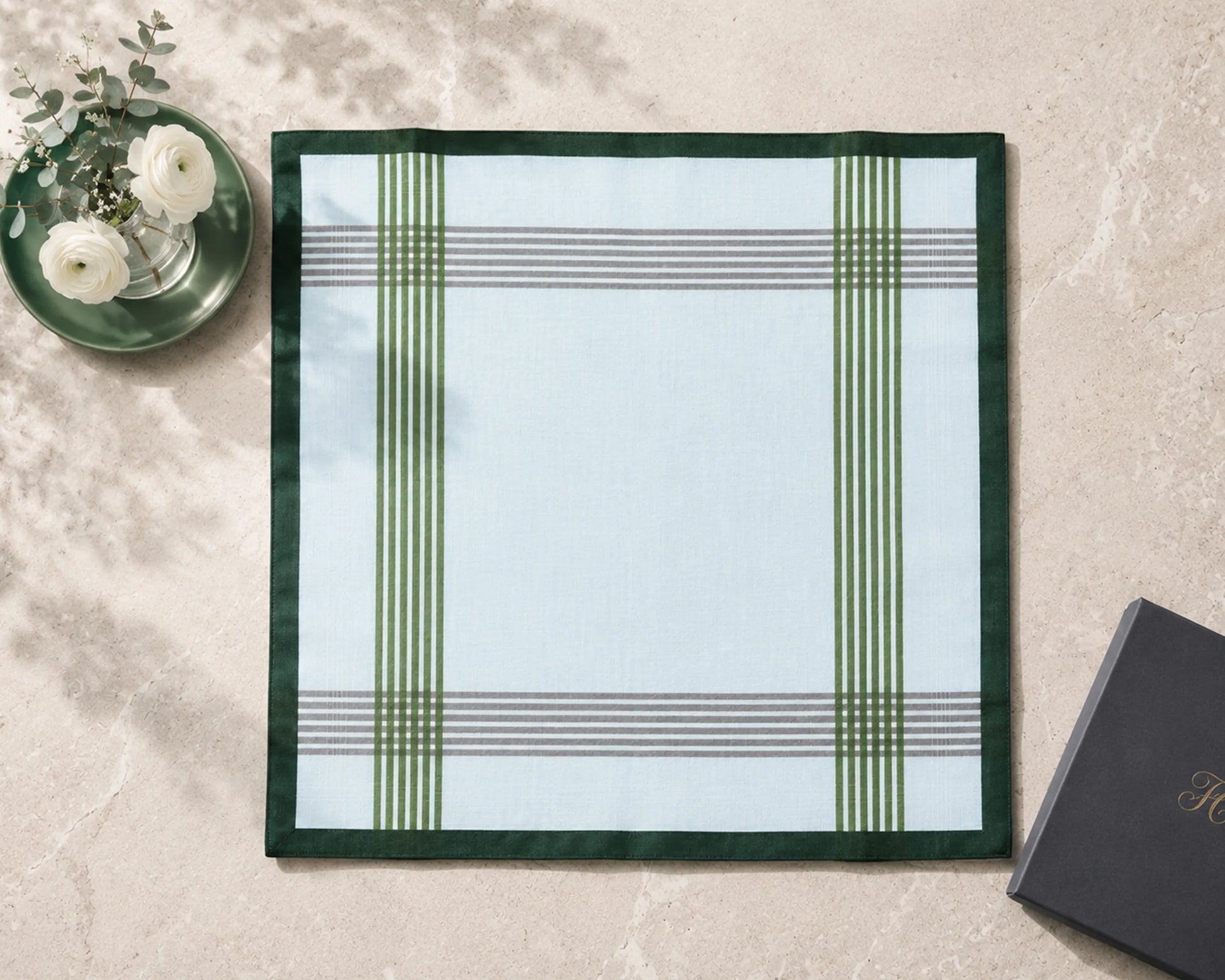 Plaid placemat on a marble surface with a black book and white flowers.