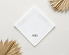 A white cotton handkerchief with a striped border and custom black monogram tucked into a navy suit pocket.