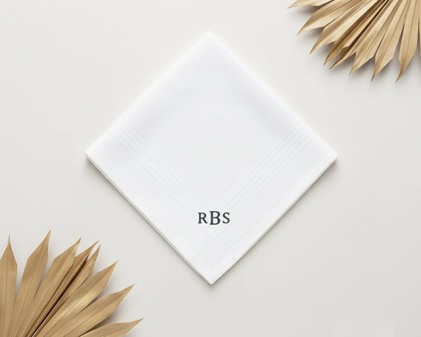 A white cotton handkerchief with a striped border and custom black monogram tucked into a navy suit pocket.