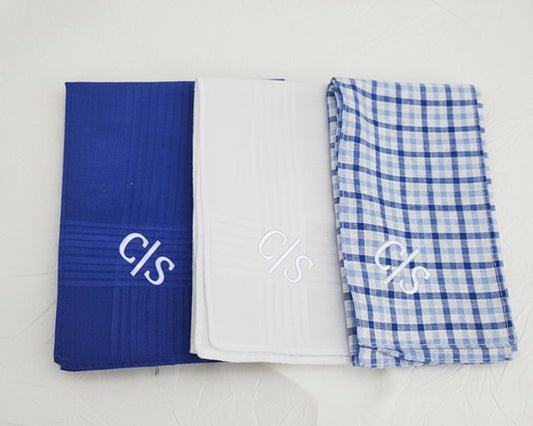 A dark gift box containing five rolled cotton handkerchiefs in navy plaid and red polka dot patterns with white RAL monograms.