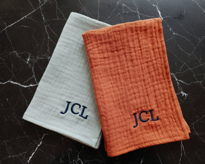 Sage green and rust orange monogrammed muslin cotton handkerchiefs displayed on a black marble surface.