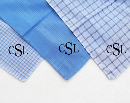 A set of three custom monogrammed pocket squares in blue and grey patterns displayed in a gift box.
