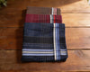 Two folded fabric swatches on a wooden surface, one brown and red striped, the other blue with white stripes.