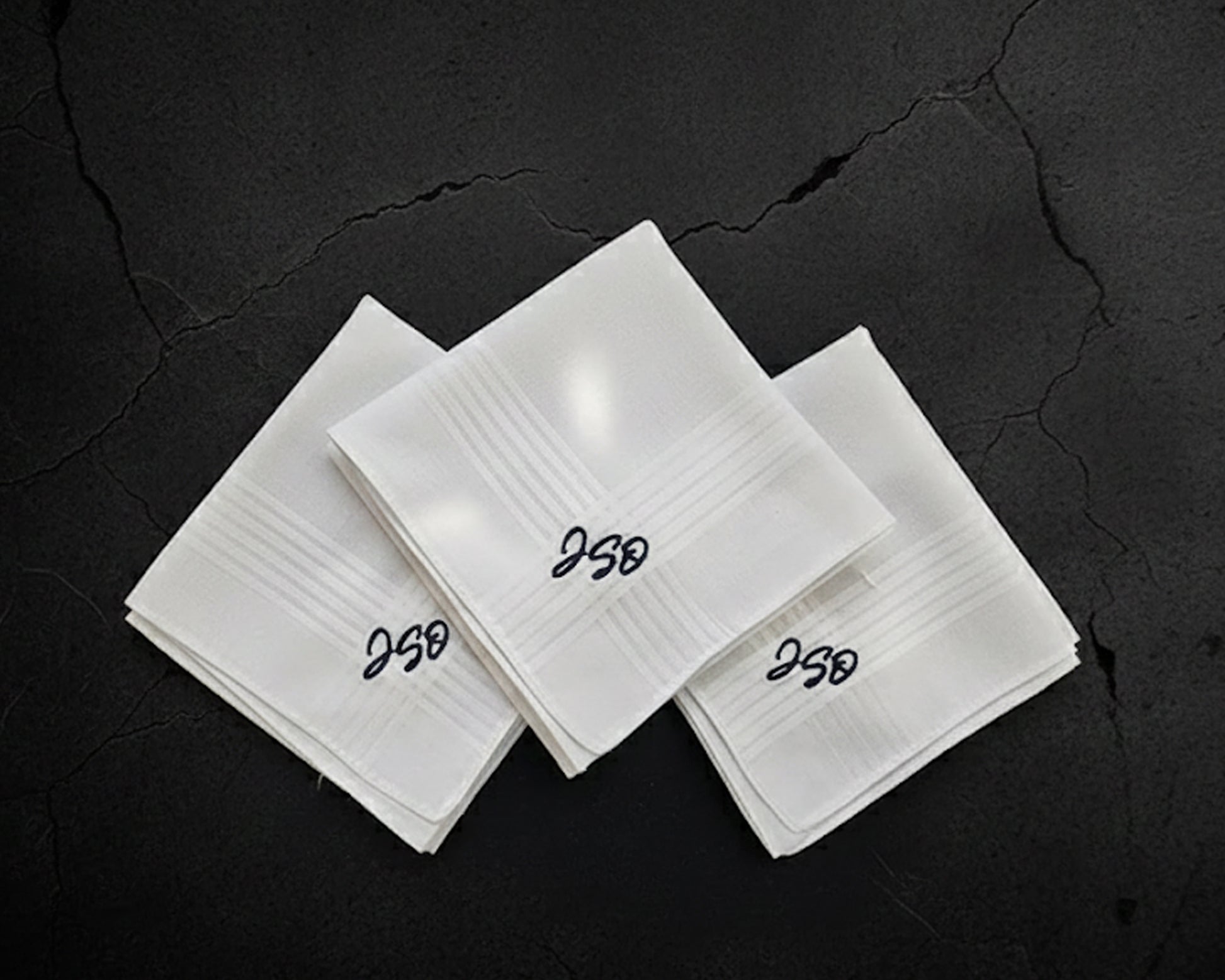 Three white folded cotton handkerchiefs with custom black script monograms 