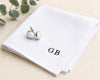 White cufflinks on a white napkin with 'GB' initials on a beige surface.