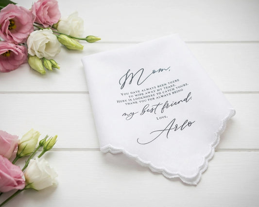 White handkerchief with personalized message surrounded by pink and white flowers on a wooden surface