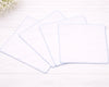 Three white rectangular placemats on a light wooden surface with a blurred floral background.