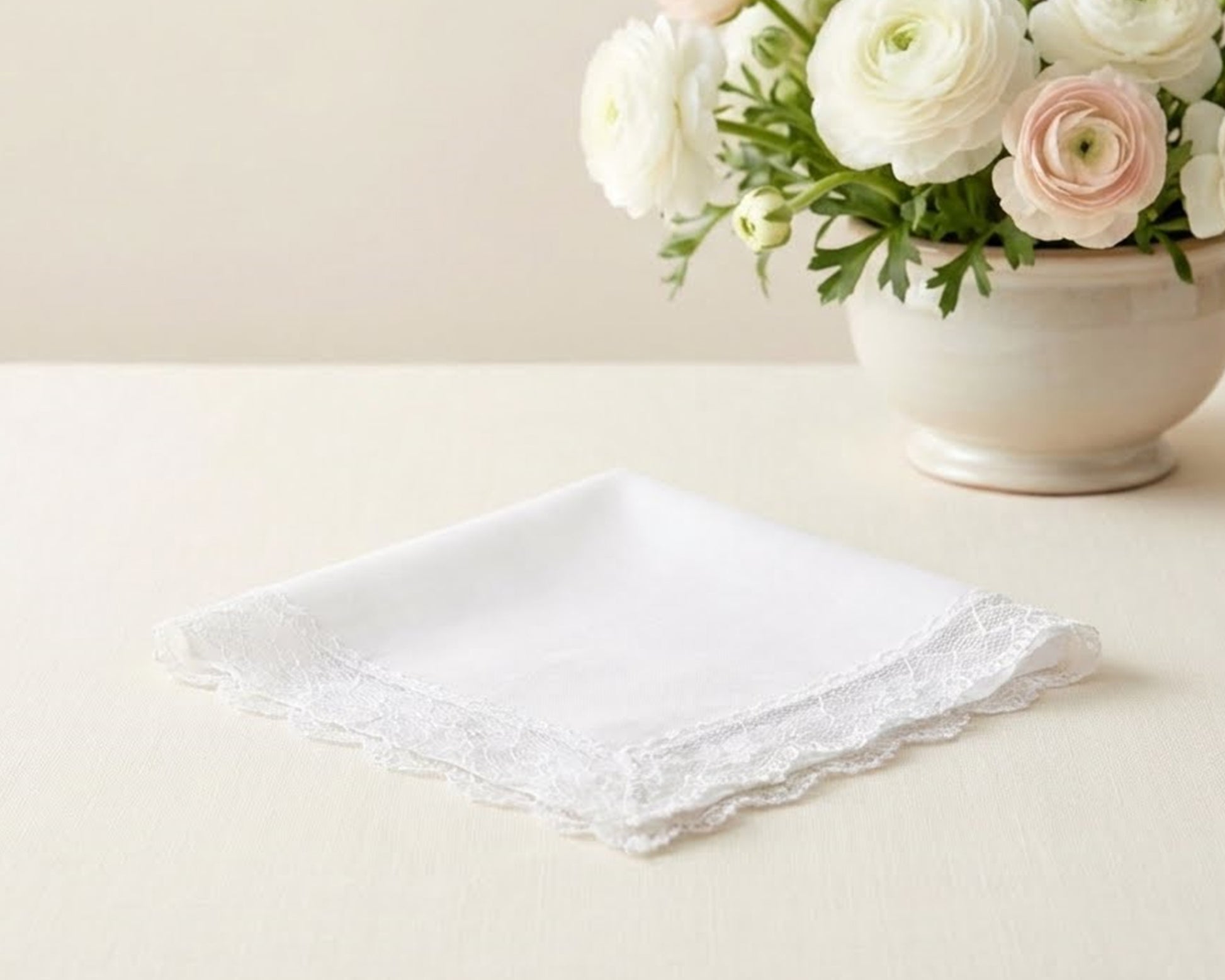 White lace handkerchief on a light surface with a vase of flowers in the background