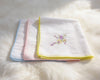 Set of folded white towels with colorful embroidery on a fluffy white surface