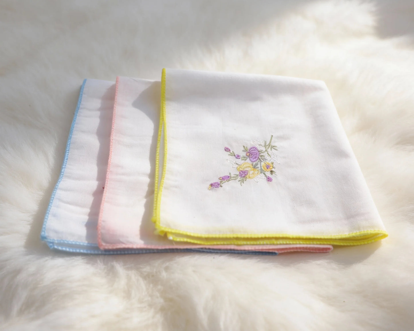 Set of folded white towels with colorful embroidery on a fluffy white surface