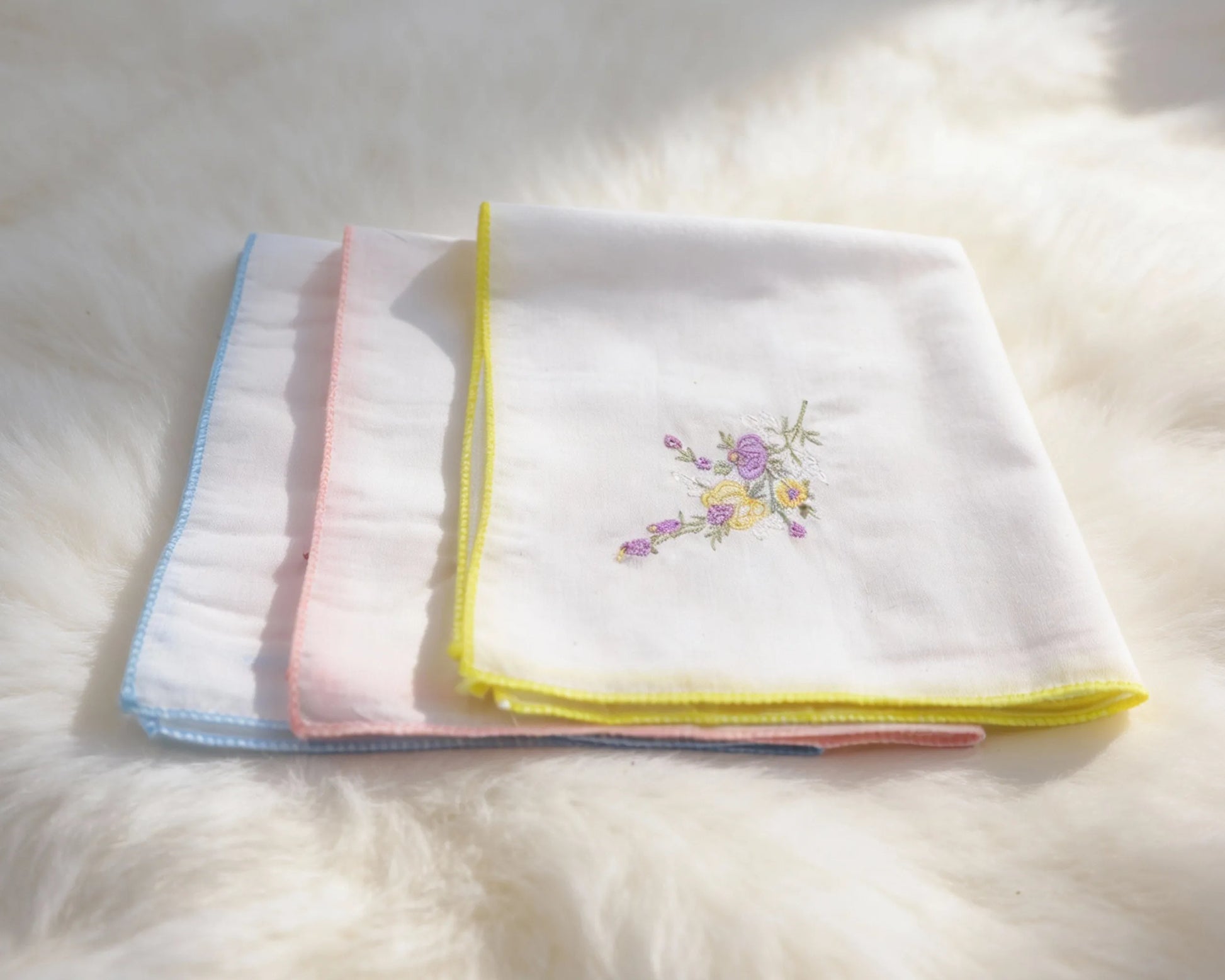 Set of folded white towels with colorful embroidery on a fluffy white surface